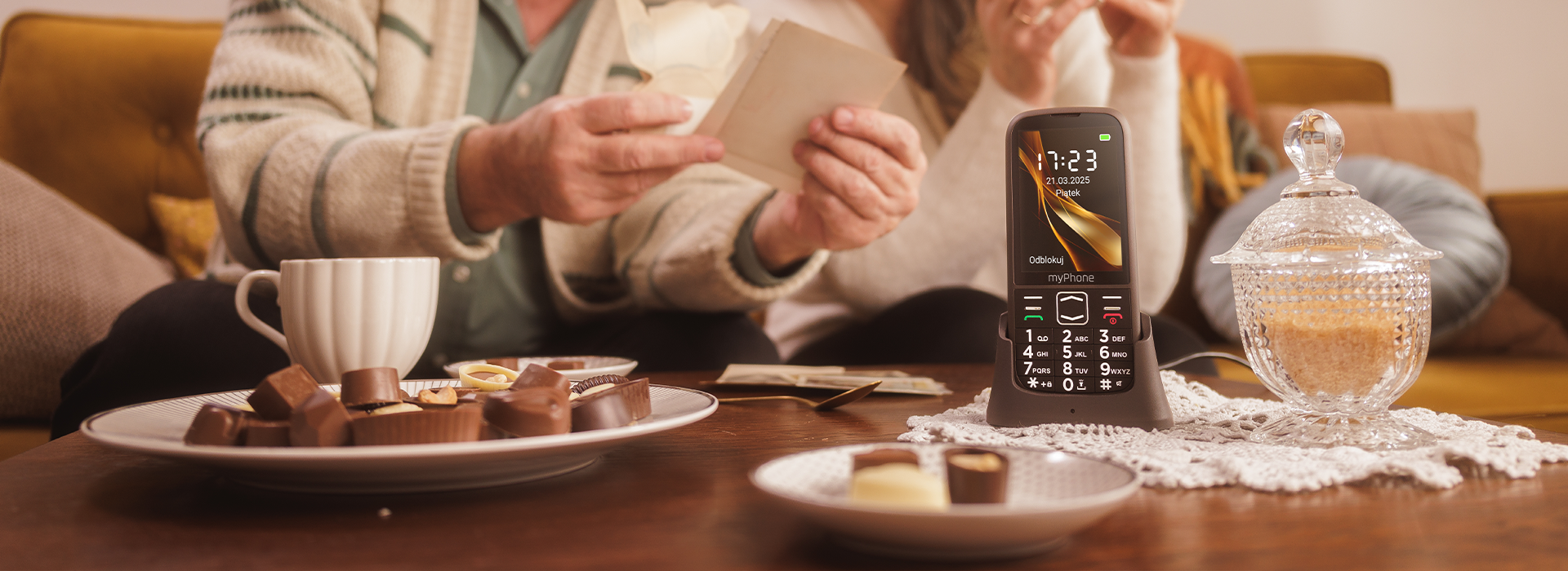 myPhone HALO 4 PLUS LTE Praline Collection Kawa herbata na stole, czekoladki starsze małżeństwo przy stole. Kryształowa cukiernica.